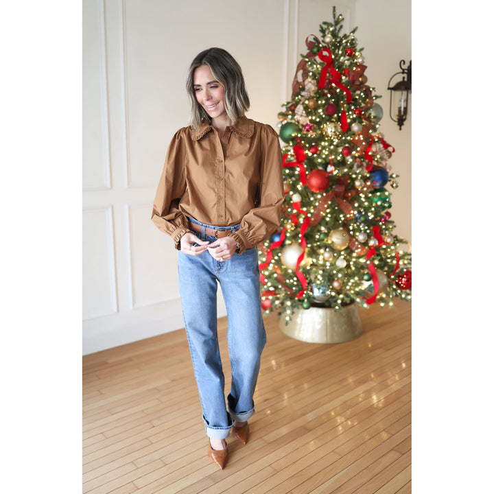 Woman in a brown shirt and blue jeans standing in front of a decorated Christmas tree.