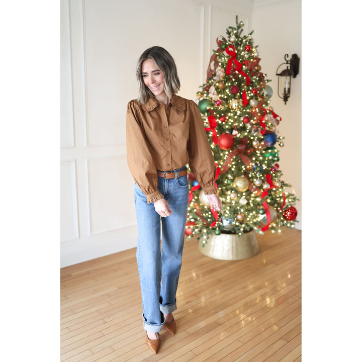 Woman in a brown shirt and blue jeans standing in front of a decorated Christmas tree.