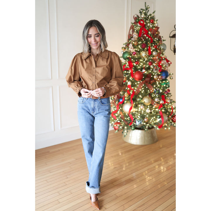 Woman in a brown blouse and blue jeans standing in front of a decorated Christmas tree.