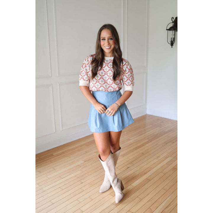 Woman wearing a patterned sweater, light blue skirt, and white knee-high boots 