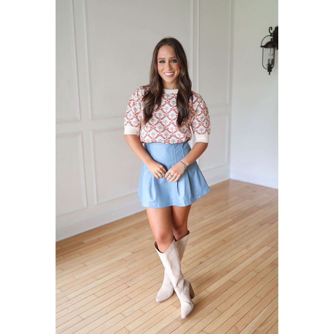 Woman wearing a patterned top, light blue skirt, and knee-high boots