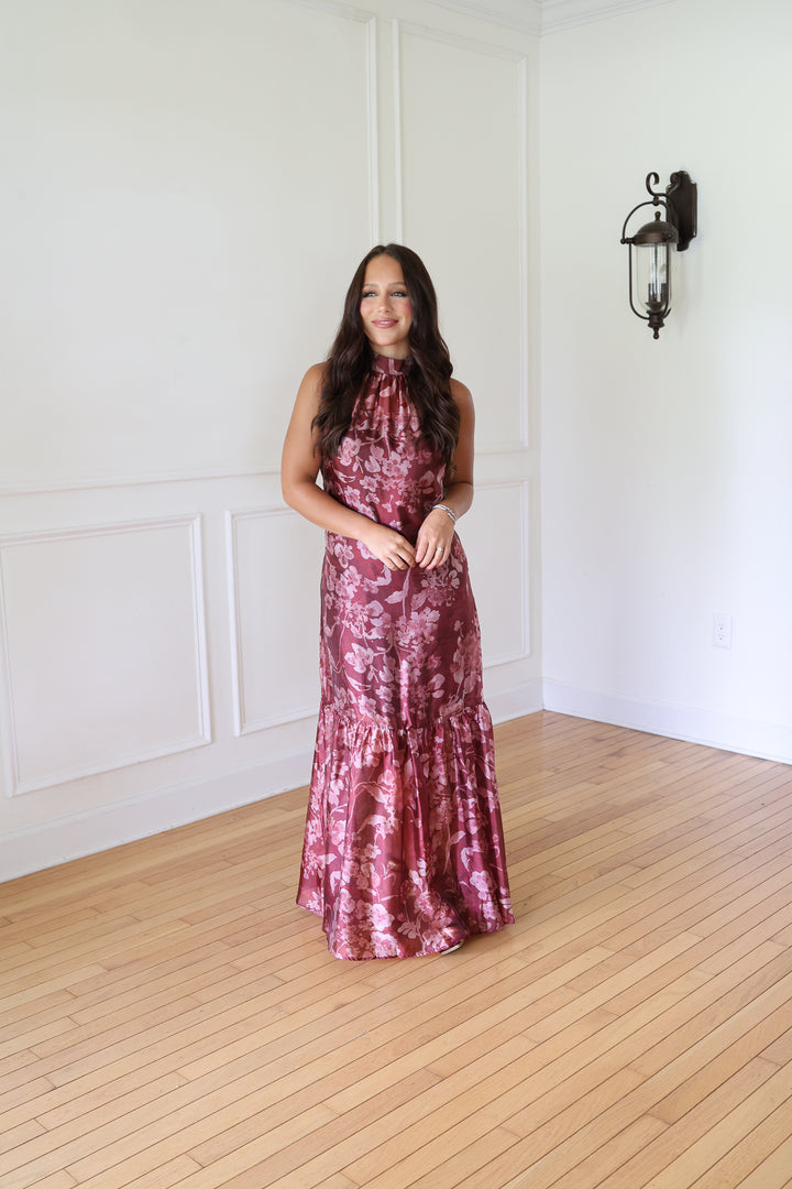 A woman wearing a sleeveless, high-neck, floor-length mermaid gown with a metallic rose gold floral pattern