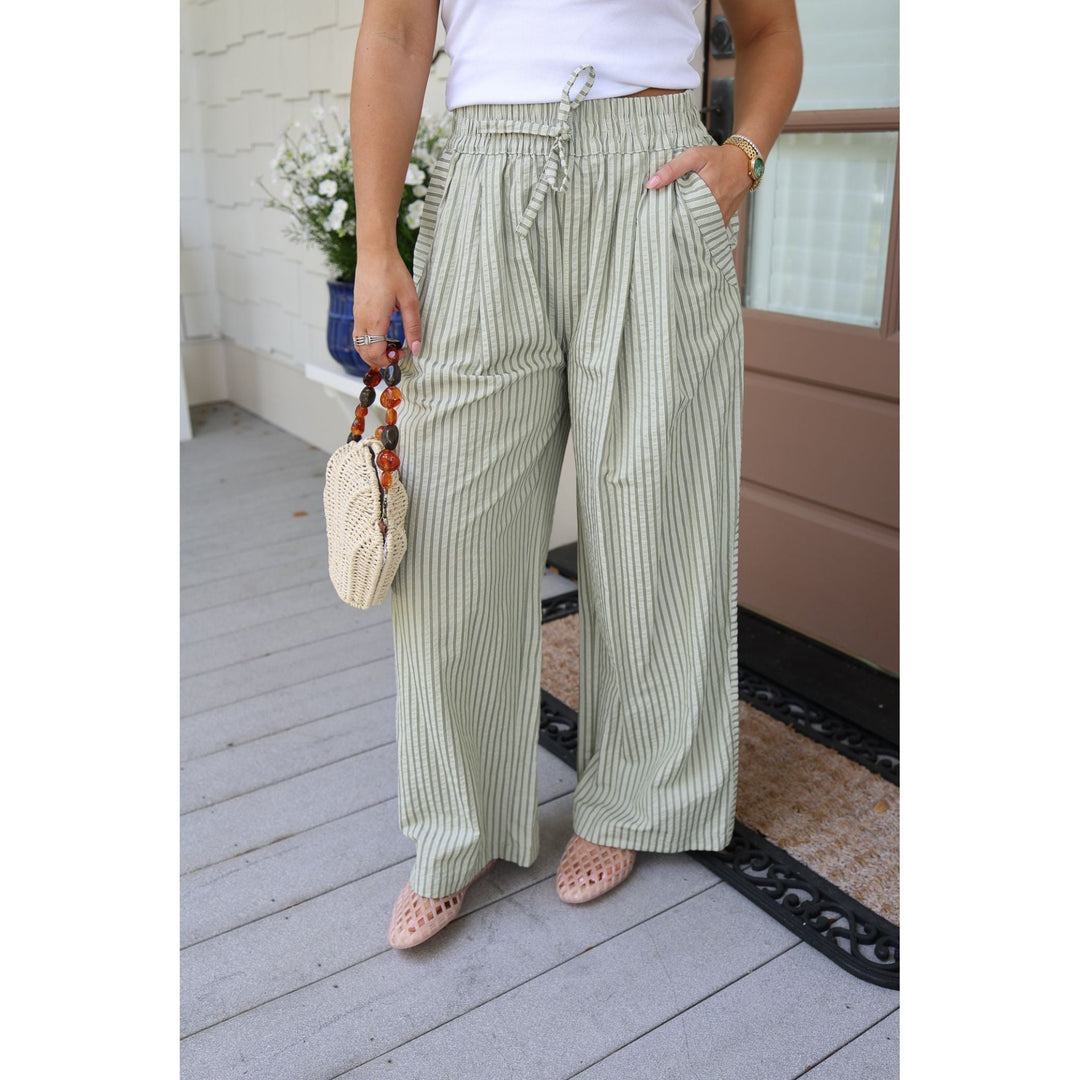 Person wearing green striped pants and a white top, standing on a wooden deck.