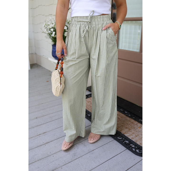 Person wearing green striped pants and a white top, standing on a wooden deck.