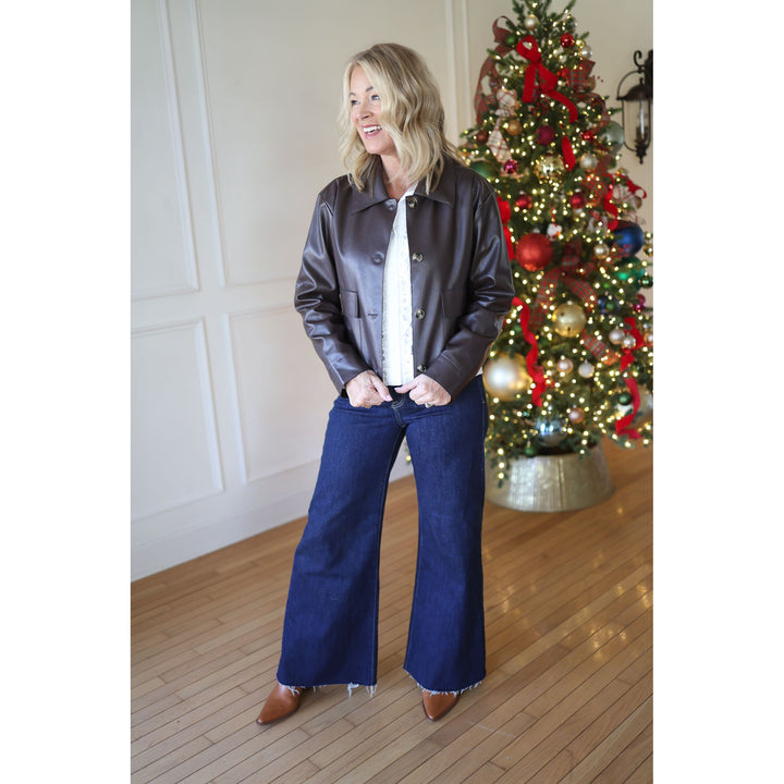 Woman in a dark jacket and blue jeans standing in front of a decorated Christmas tree.