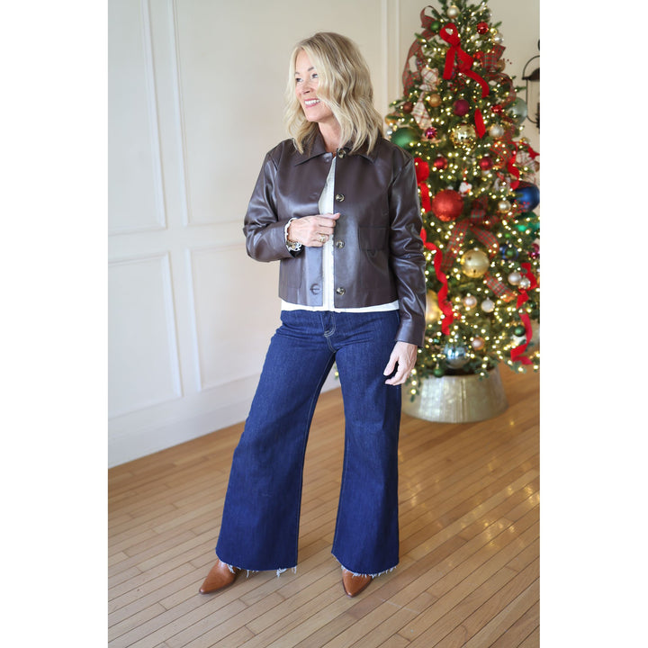 Woman in a leather jacket and blue jeans standing in front of a decorated Christmas tree.