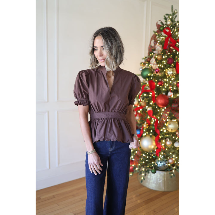 Woman in a brown top and blue jeans standing in front of a decorated Christmas tree.
