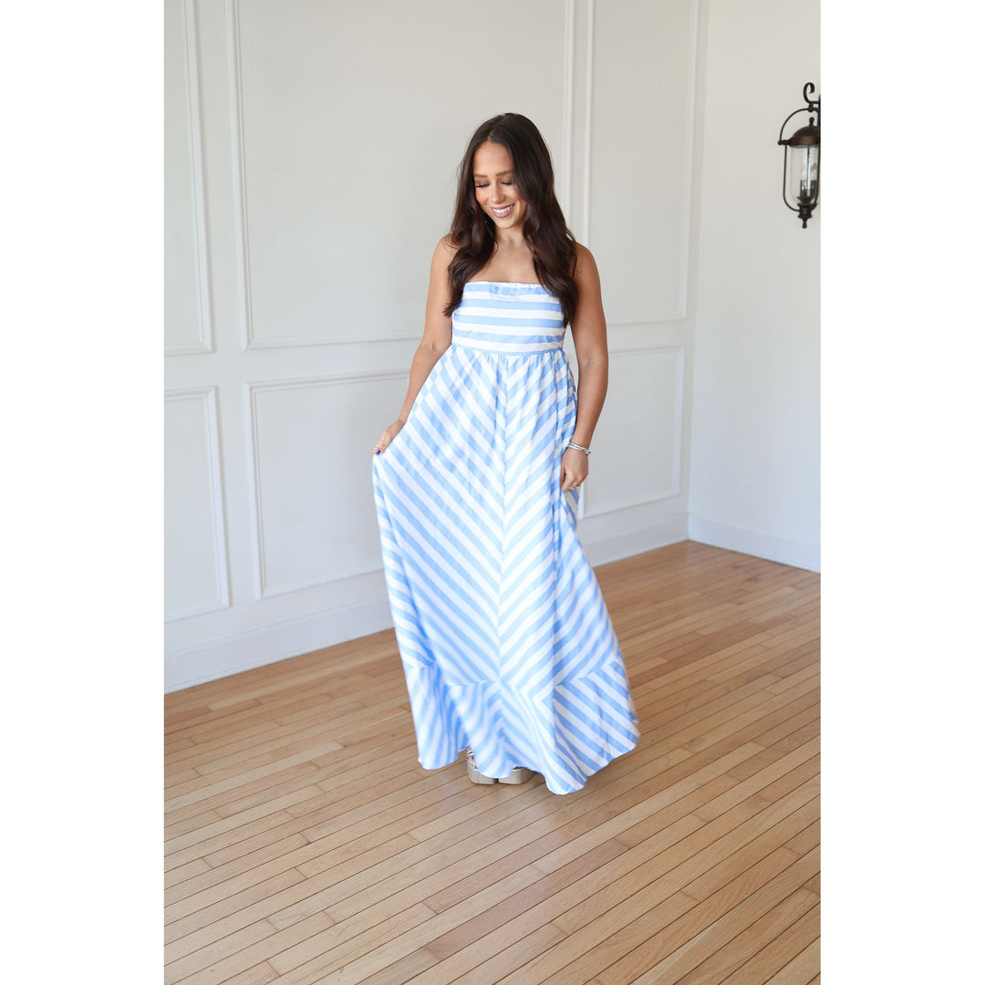 Woman wearing a blue and white striped dress standing in a room with wooden flooring and white walls.