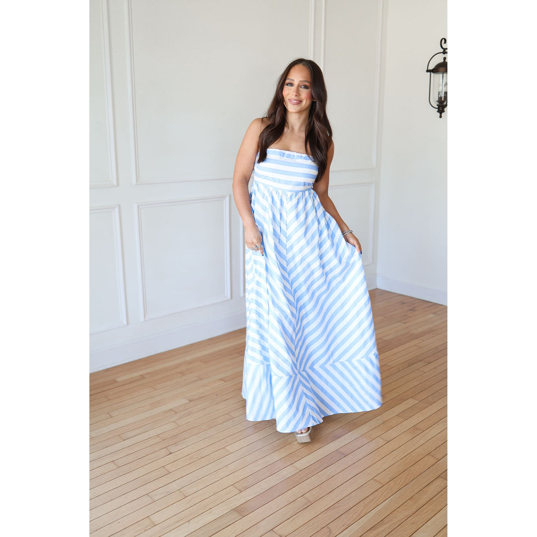 Woman wearing a blue and white striped dress standing in a room with wooden flooring and white walls.