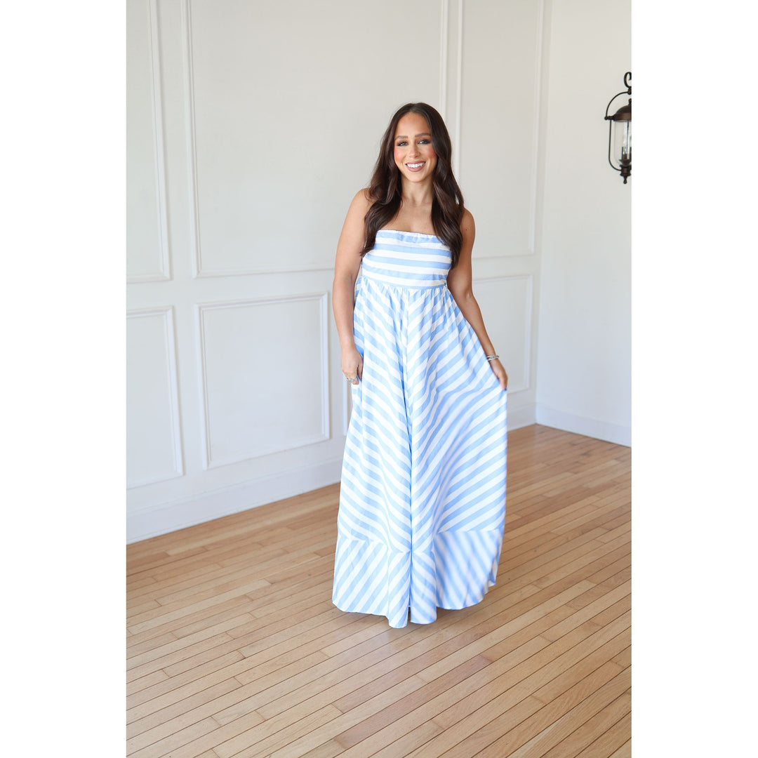 Woman wearing a blue and white striped dress standing in a room with wooden flooring and white walls.