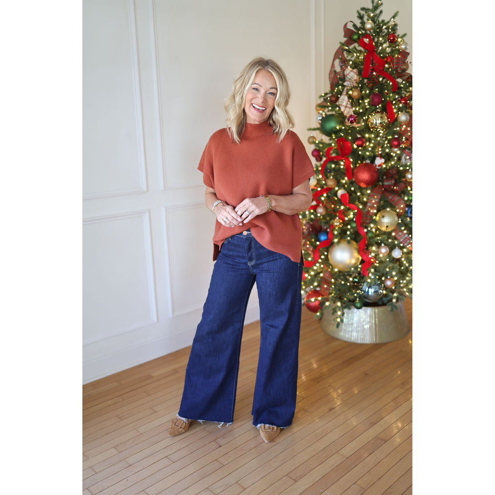 Woman in a rust-colored top and blue jeans standing next to a decorated Christmas tree.