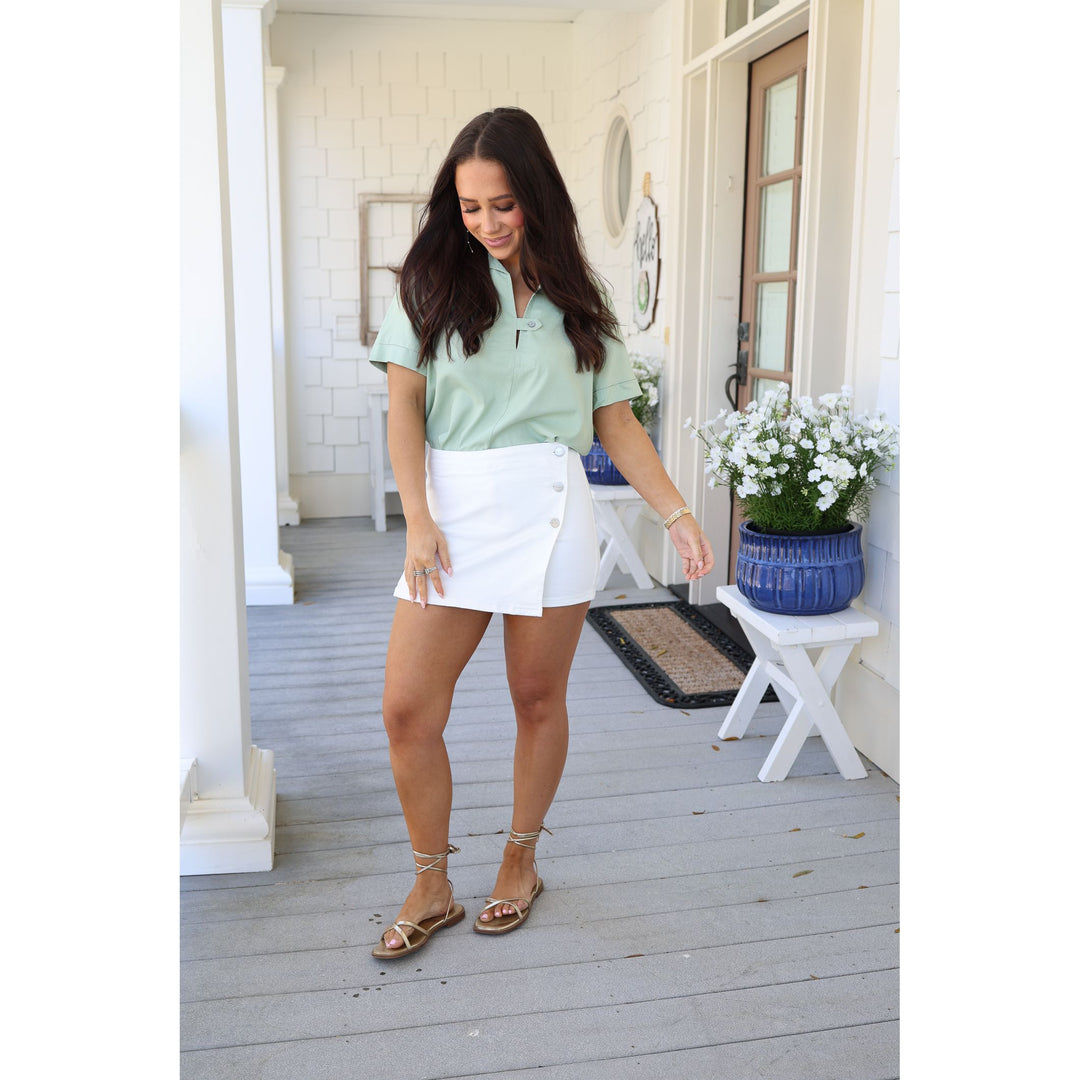 Woman in a light green polo shirt and white skirt standing on a wooden deck.