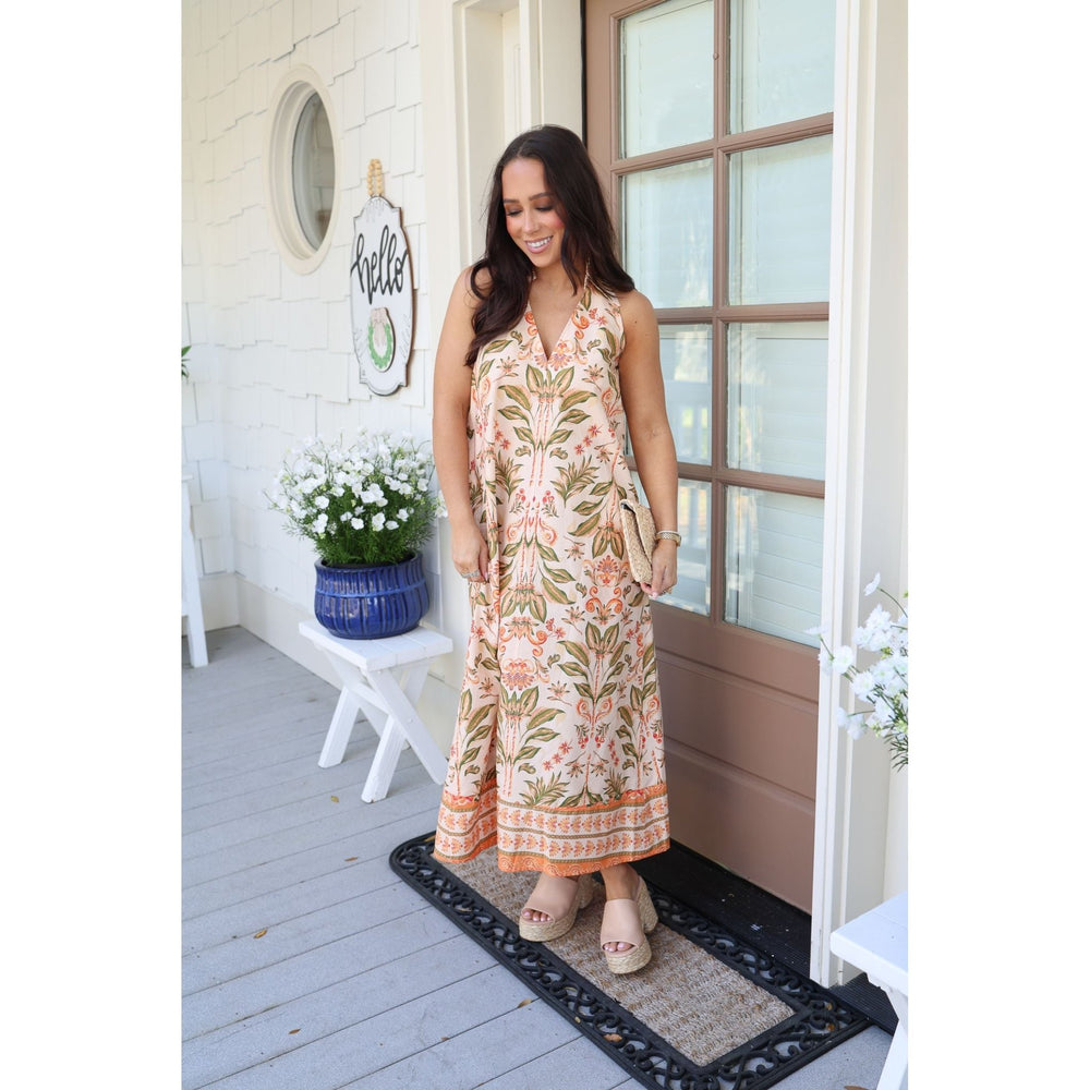 Woman in a floral dress standing on a porch with plants and a 'Hello' sign.