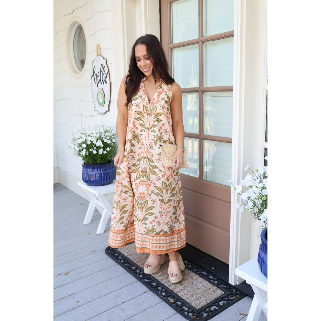 Woman in a floral dress standing on a porch with flowers and a welcome sign.