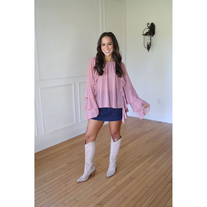 Woman wearing a pink blouse, blue skirt, and white knee-high boots 