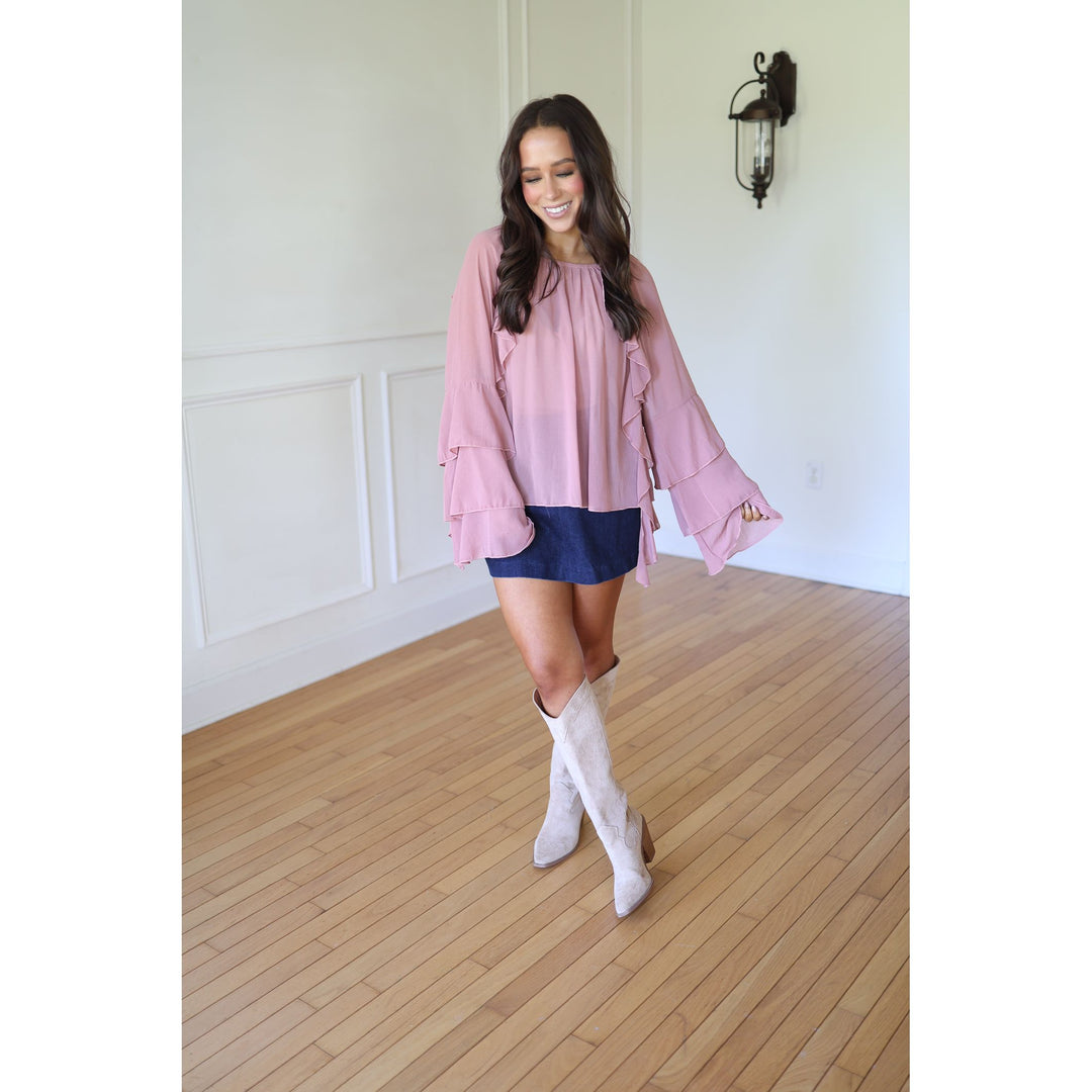 Woman wearing a pink blouse, blue skirt, and white boots 