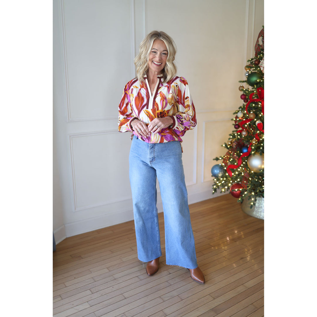 Woman in a colorful blouse and blue jeans standing in front of a decorated Christmas tree.
