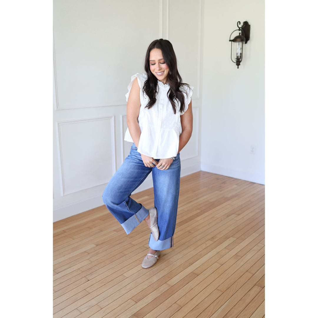 Woman in a white blouse and blue jeans standing on a wooden floor.