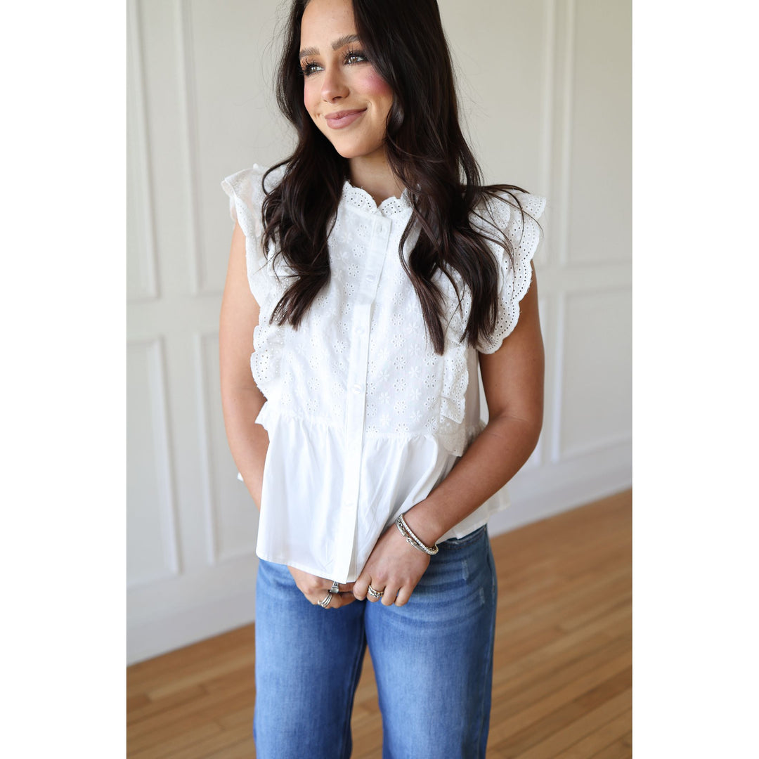 Woman wearing a white blouse with lace details and blue jeans indoors.