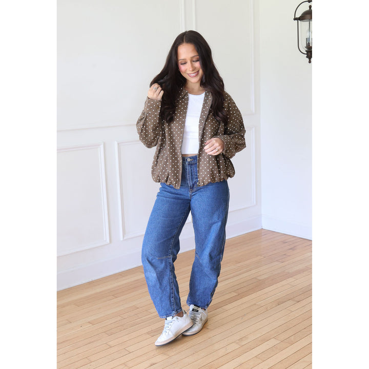 A woman modeling a brown sheer polka-dot jacket over a white top, paired with blue jeans and white sneakers