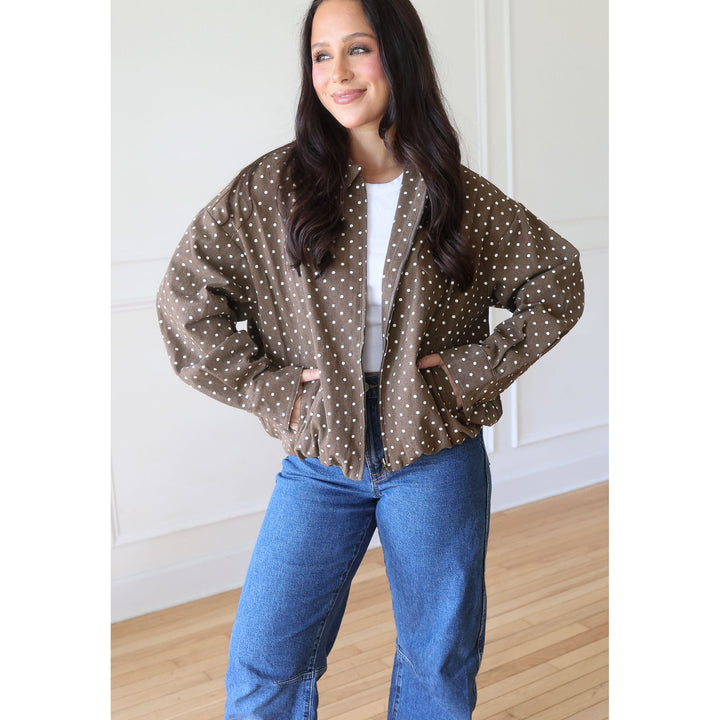 A woman modeling a brown and white polka dot bomber jacket, paired with a white t-shirt and blue jeans