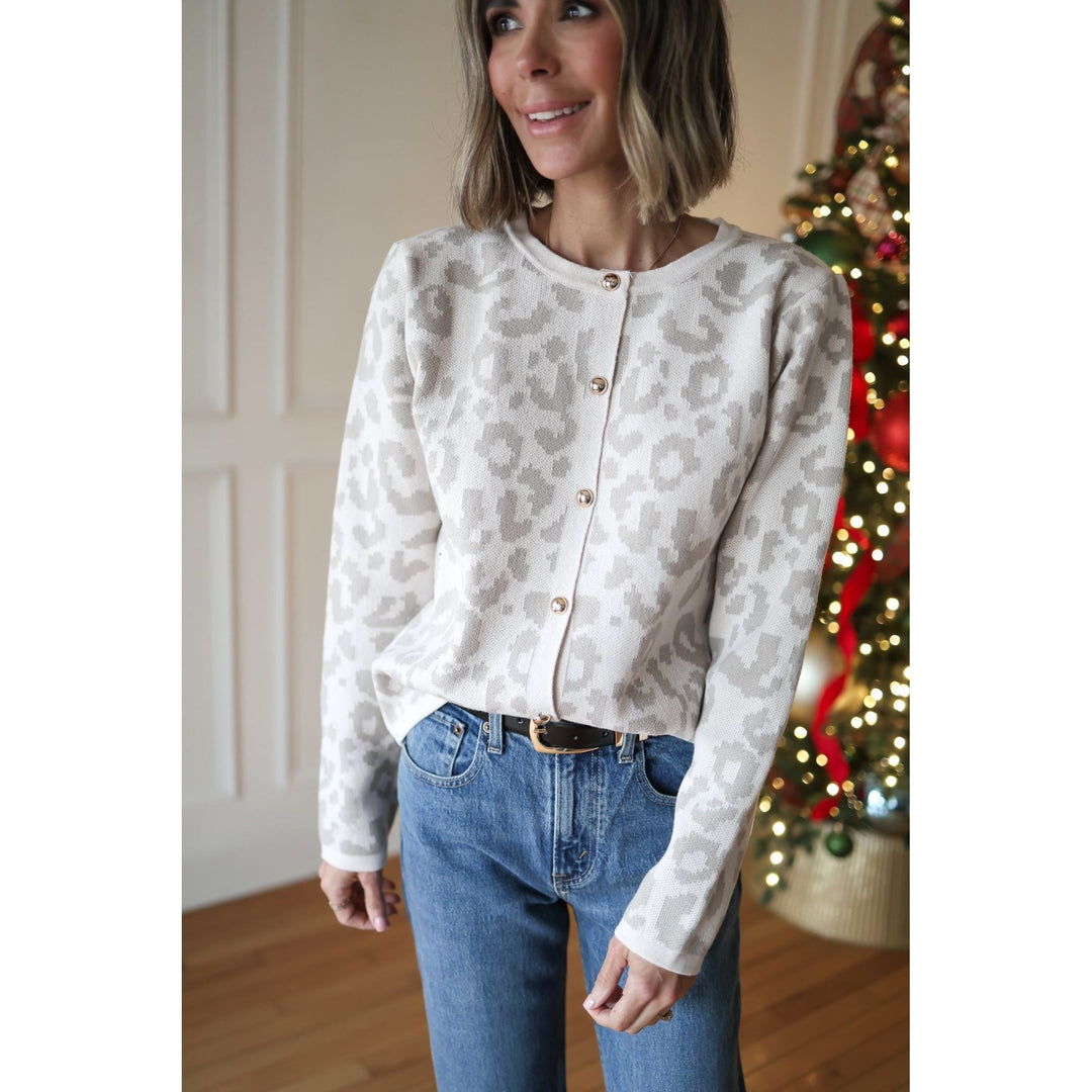 Woman wearing a patterned cardigan and jeans standing in front of a decorated Christmas tree.