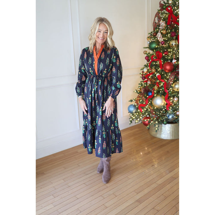 Woman in a navy dress standing next to a decorated Christmas tree indoors.