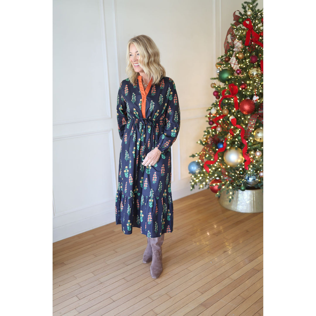 Woman in a navy dress standing next to a decorated Christmas tree indoors.