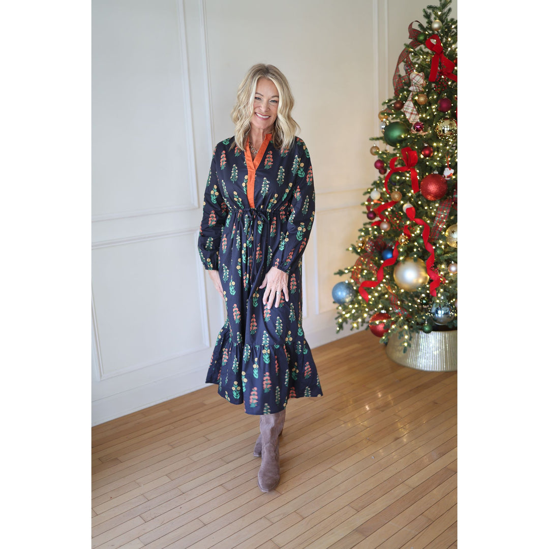 Woman in a navy dress standing next to a decorated Christmas tree indoors.