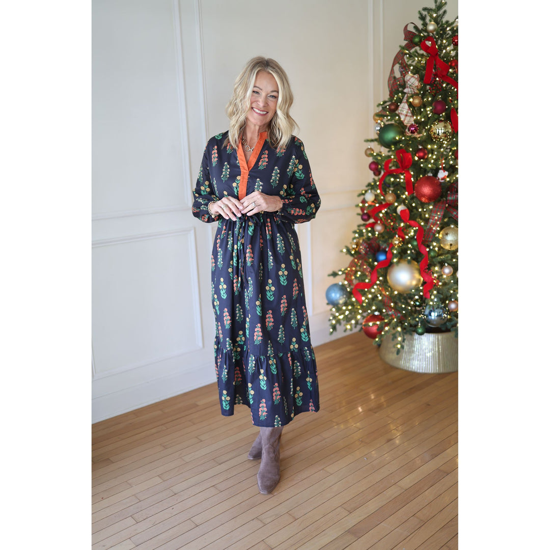 Woman in a navy floral dress standing next to a decorated Christmas tree indoors.