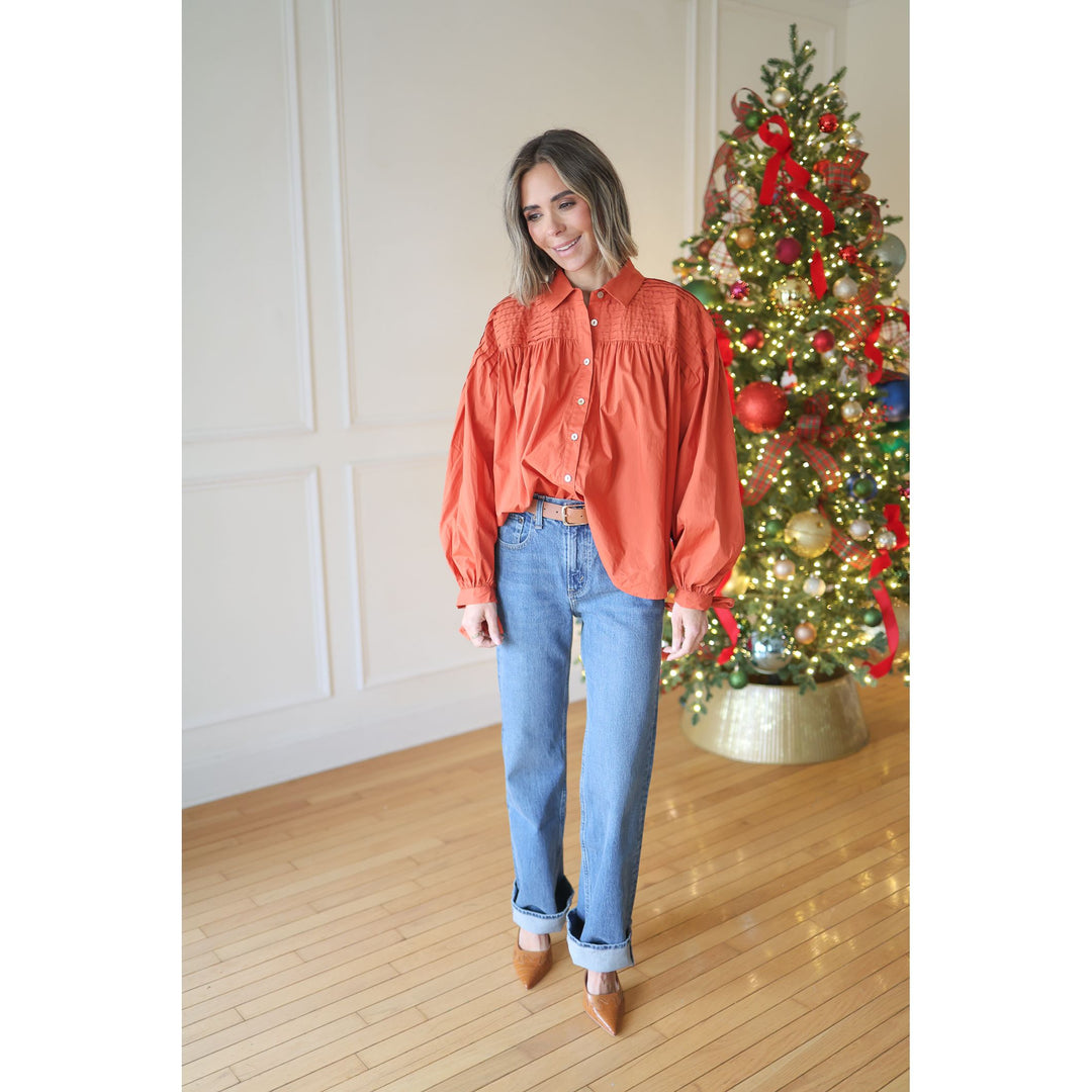 Woman in an orange blouse and blue jeans standing in front of a decorated Christmas tree.
