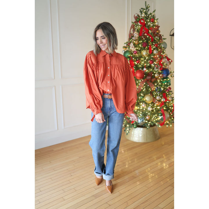 Woman in an orange blouse and blue jeans standing in front of a decorated Christmas tree.