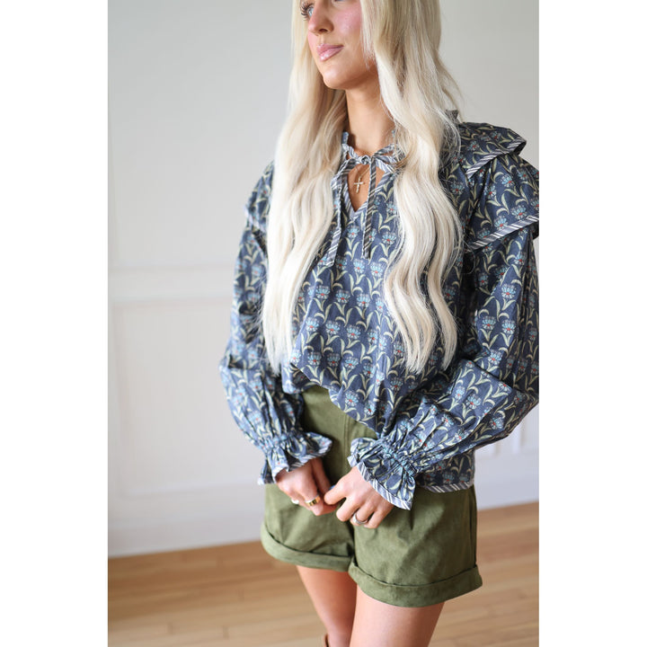 Woman wearing a blue floral blouse and green shorts indoors.