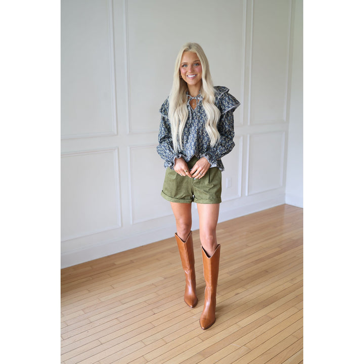 Woman wearing a patterned blouse, green shorts, and brown knee-high boots 
