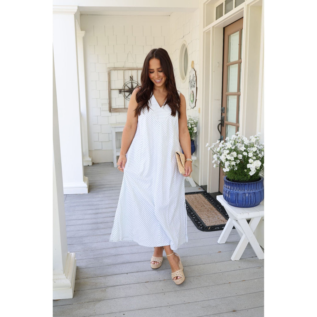 Woman in a white dress standing on a porch with a plant and table in the background