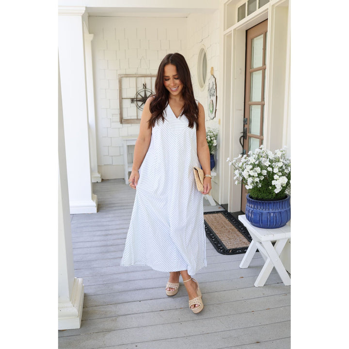 Woman in a white dress standing on a porch with a plant and table in the background