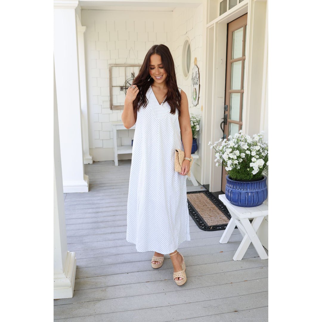 Woman in a white dress standing on a porch with a plant and table.