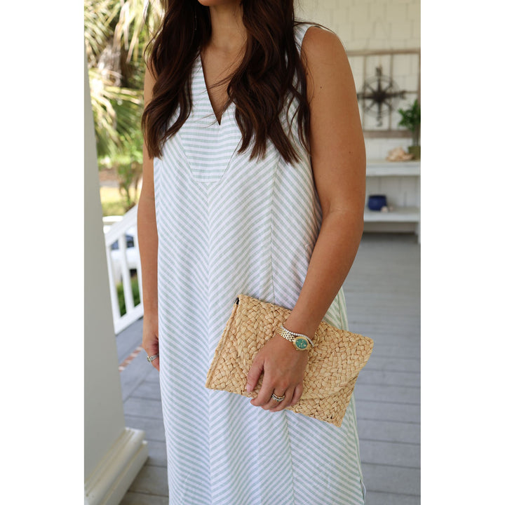 Woman in a white dress holding a straw clutch on a wooden deck.