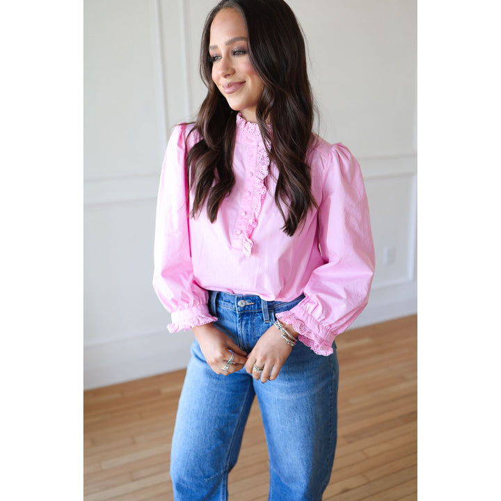 Woman wearing a pink blouse with ruffled details and blue jeans indoors.