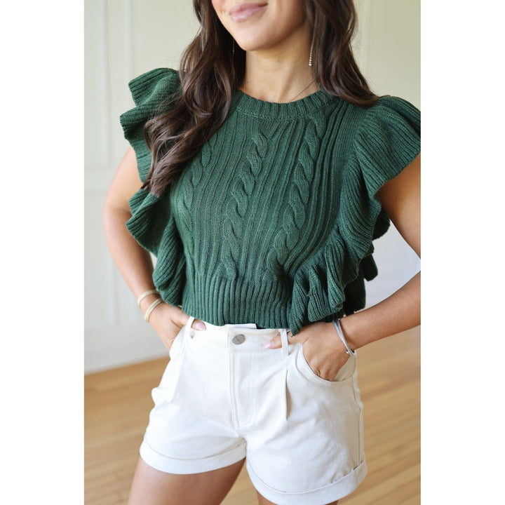 Person wearing a green cable knit top with ruffled sleeves and white shorts 