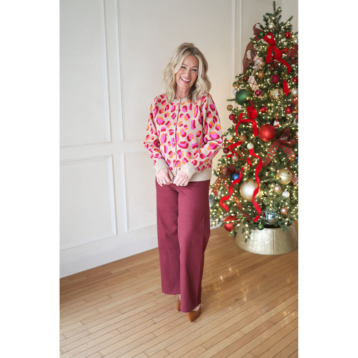 Woman in a colorful sweater and maroon pants standing next to a decorated Christmas tree.