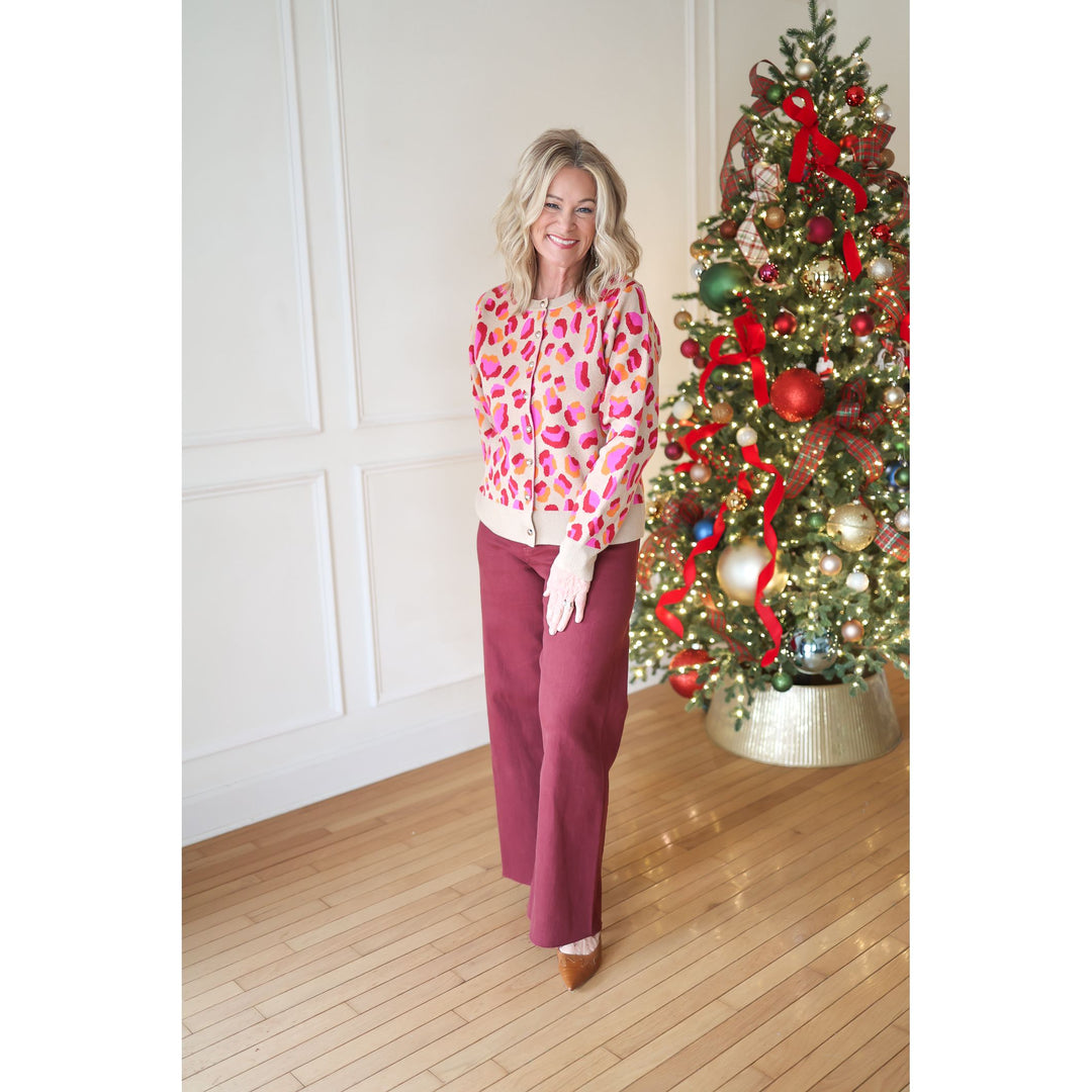 Woman in a colorful blouse and red pants standing next to a decorated Christmas tree.