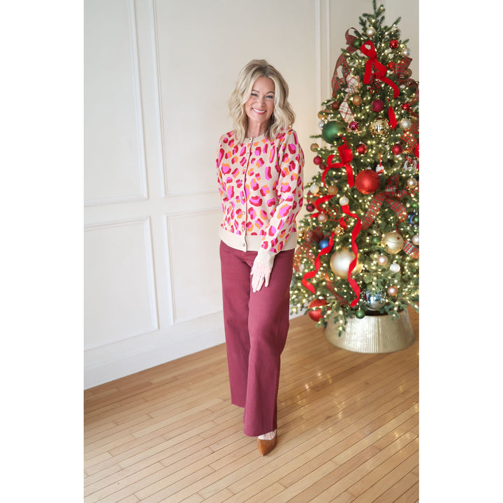 Woman in a colorful blouse and red pants standing next to a decorated Christmas tree.