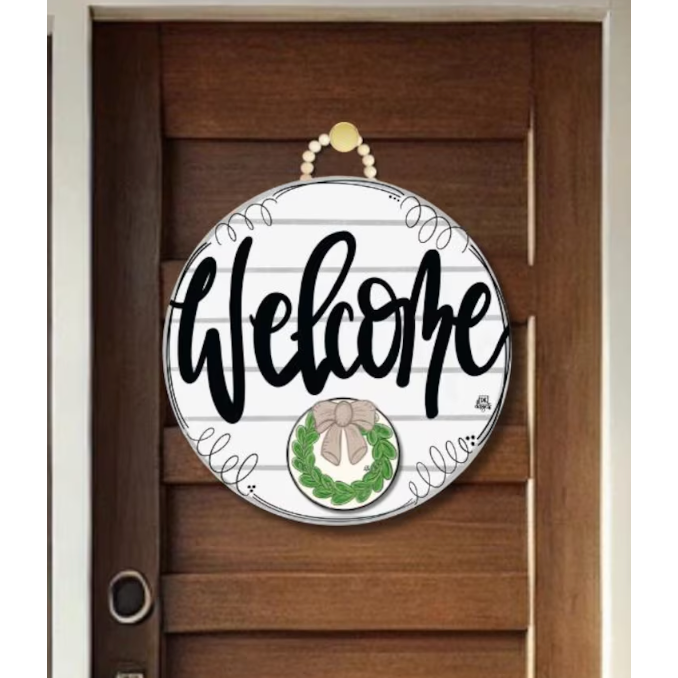 Round decorative sign with 'Welcome' text and wreath design on a wooden door.