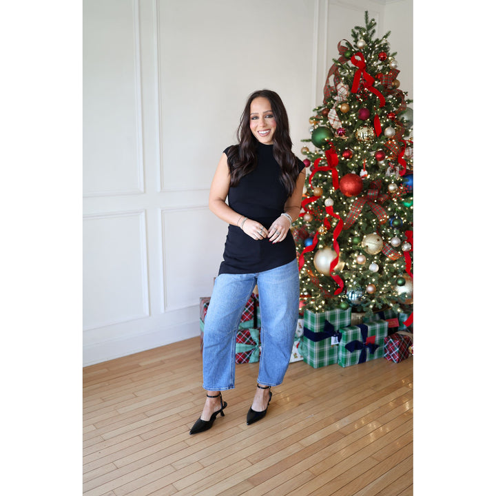 Woman standing in front of a decorated Christmas tree with presents underneath.