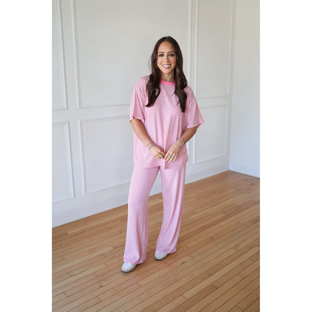 Woman wearing a pink outfit standing in a room with wooden flooring and white walls.