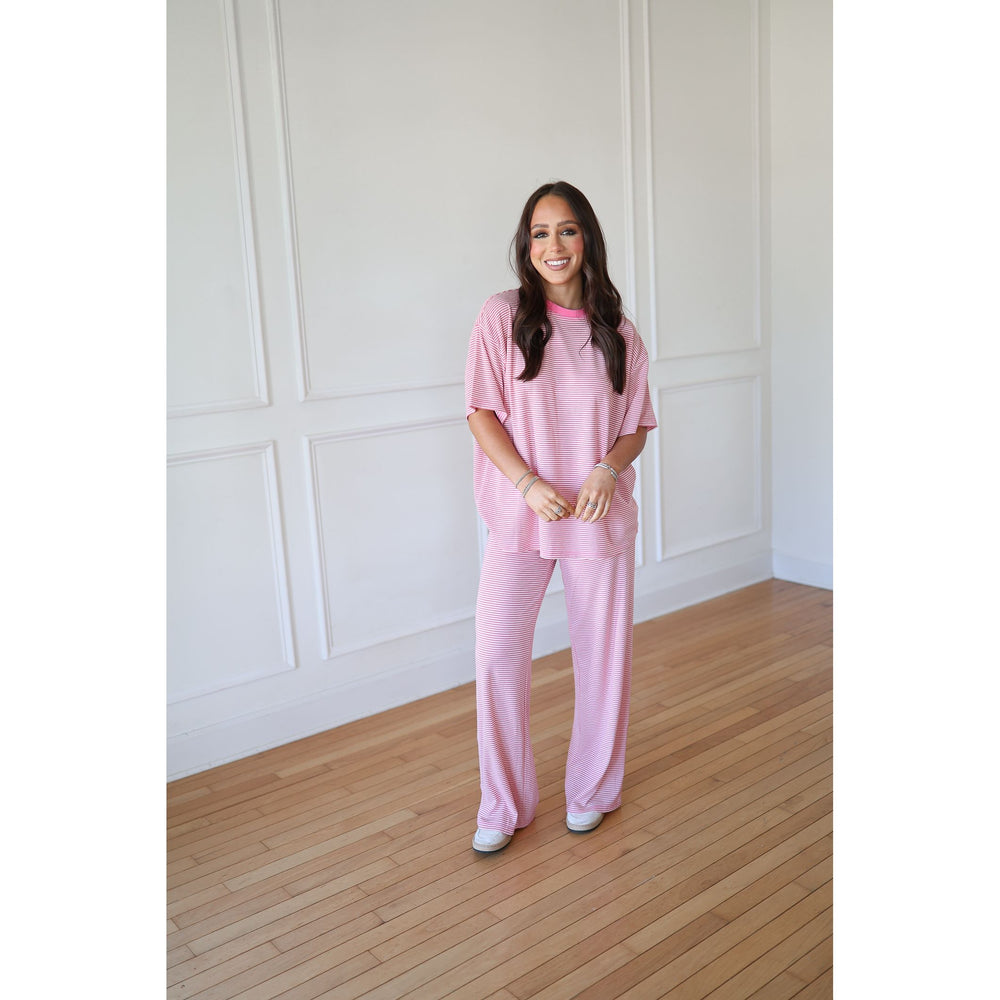 Woman wearing a pink outfit standing in a room with white paneled walls and wooden flooring.