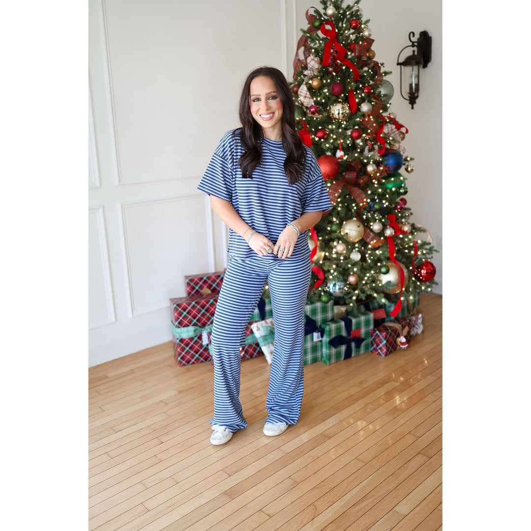 Woman in blue striped outfit standing in front of a decorated Christmas tree with presents.