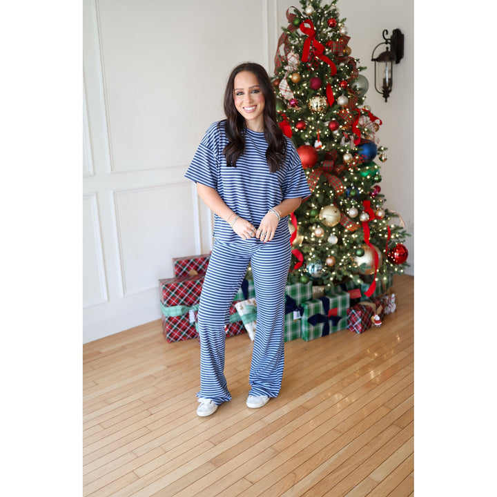 Woman in blue striped outfit standing in front of a decorated Christmas tree with presents.