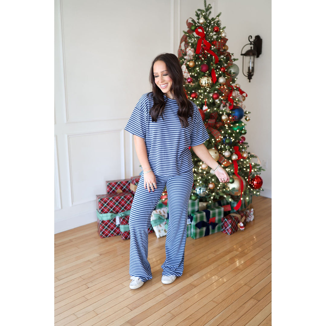 Woman in blue striped pajama set standing in front of a decorated Christmas tree.